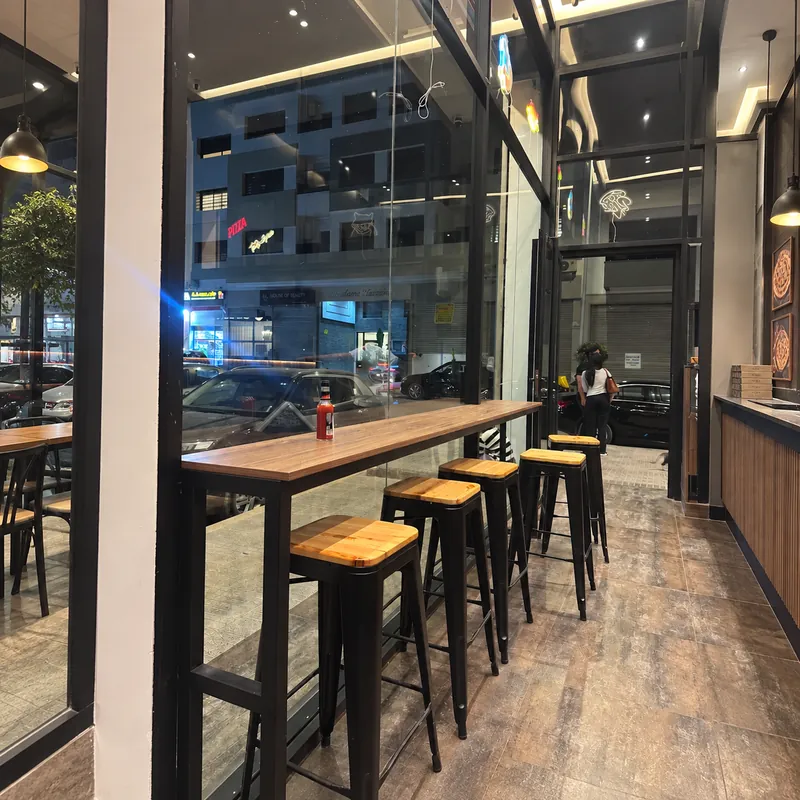 Salle vitrée d'Apollonia Pizza avec tables hautes et tabourets en bois