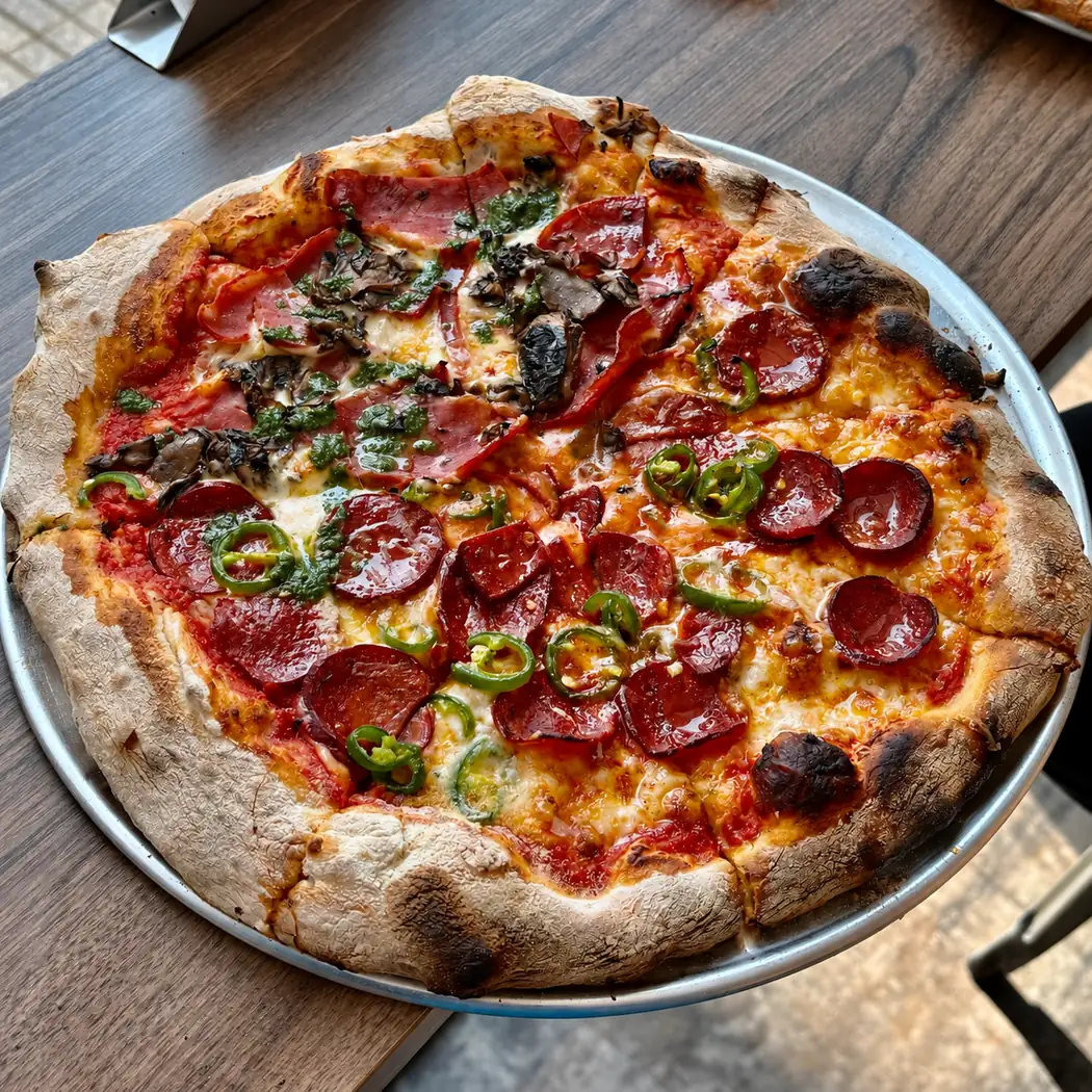 Pizza pepperoni aux piments verts et champignons servie sur plateau chez Apollonia Pizza