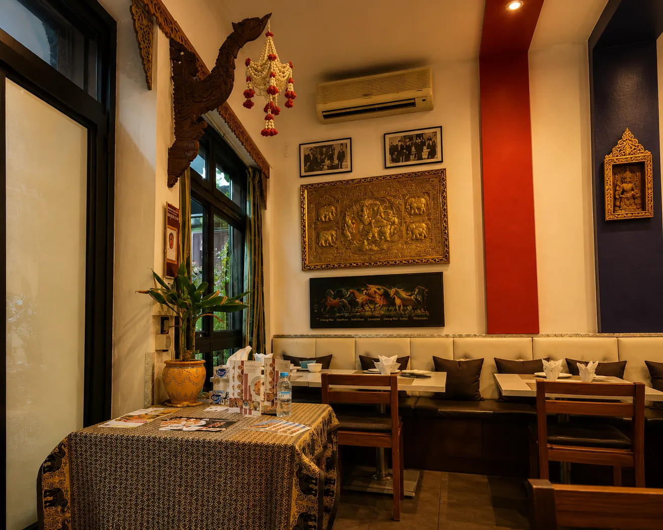 Salle du Petit Thai à Marrakech : banquette à coussins, tableaux d'éléphants dorés et tête de naga sculptée