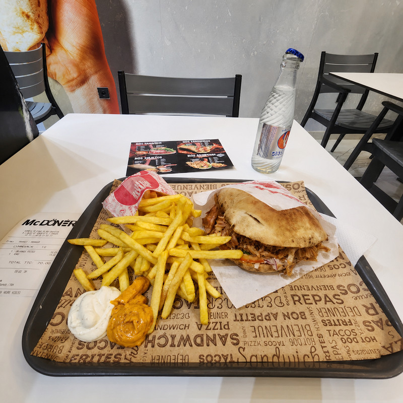 Plateau de McDöner avec sandwich döner, frites et sauces, salle claire en arrière-plan