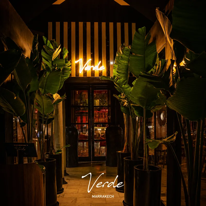 Entrée de Verde Marrakech de nuit, encadrée de grandes plantes et d'une enseigne lumineuse