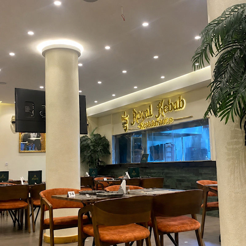 Salle de Royal Kebab Guéliz, fauteuils orange, piliers blancs et comptoir au logo doré