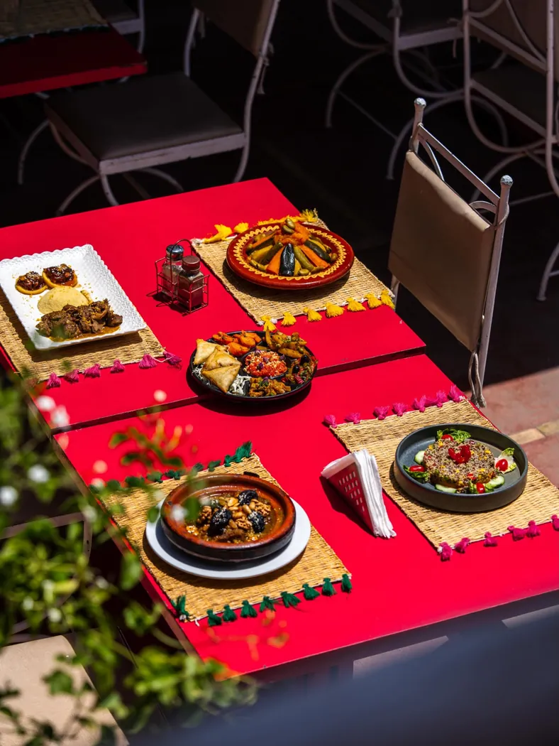 Table rouge de Kui-Zin en terrasse avec tajines, couscous et salades marocaines