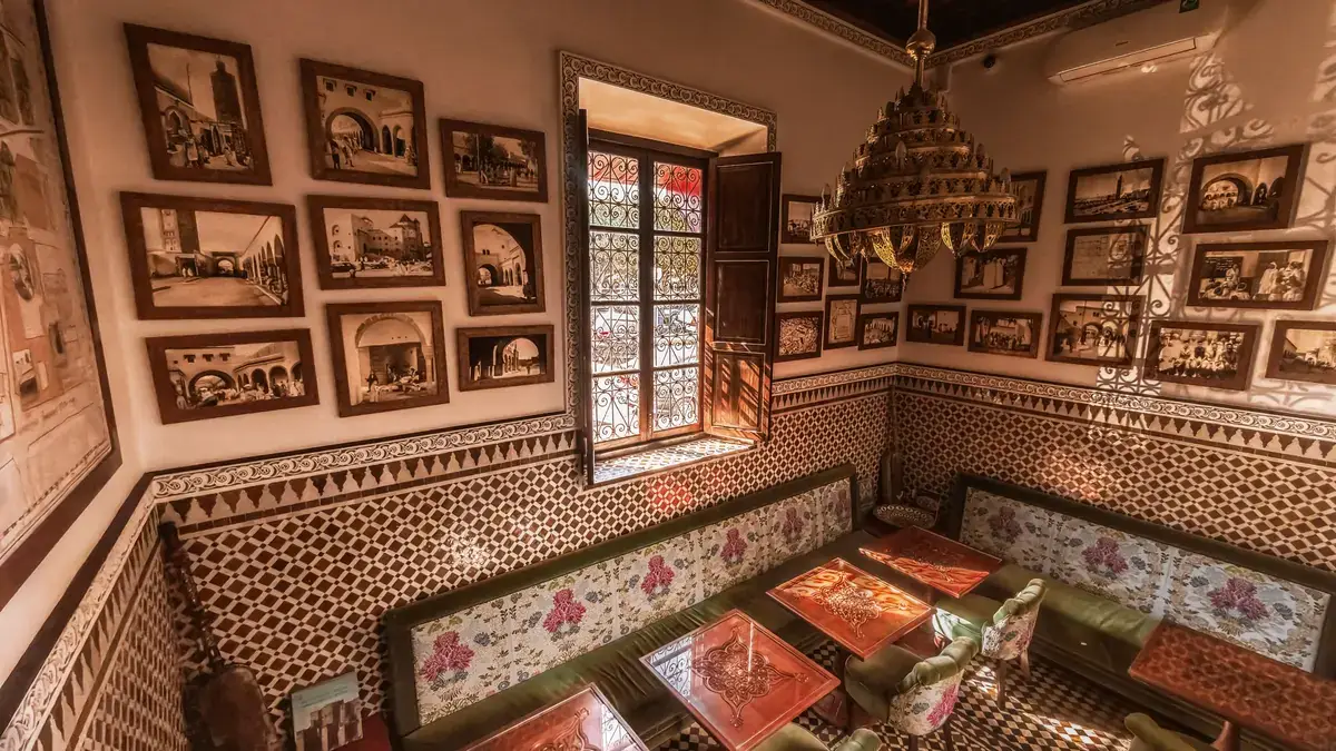 Salon marocain de MaQam avec banquettes, zelliges et murs couverts de photos anciennes