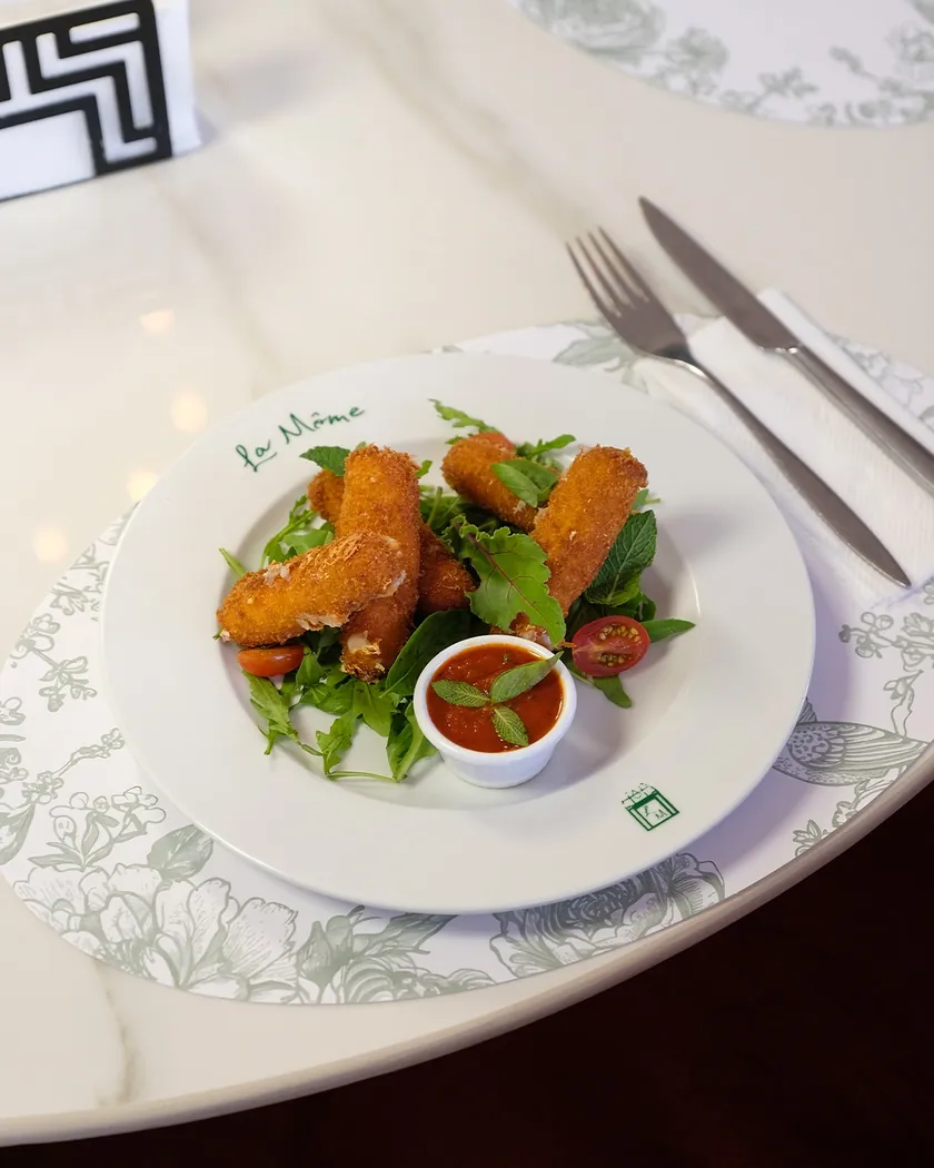 Bâtonnets panés sur salade et sauce tomate dans une assiette siglée La Môme