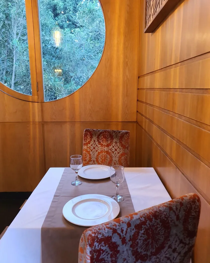 Table pour deux de Riad 21 le long de boiseries claires, face à une fenêtre ronde