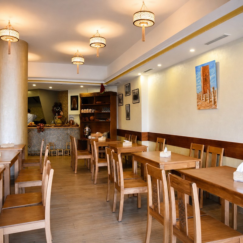 Salle lumineuse de Dar Al Achab avec suspensions en cuivre et rangée de tables en bois