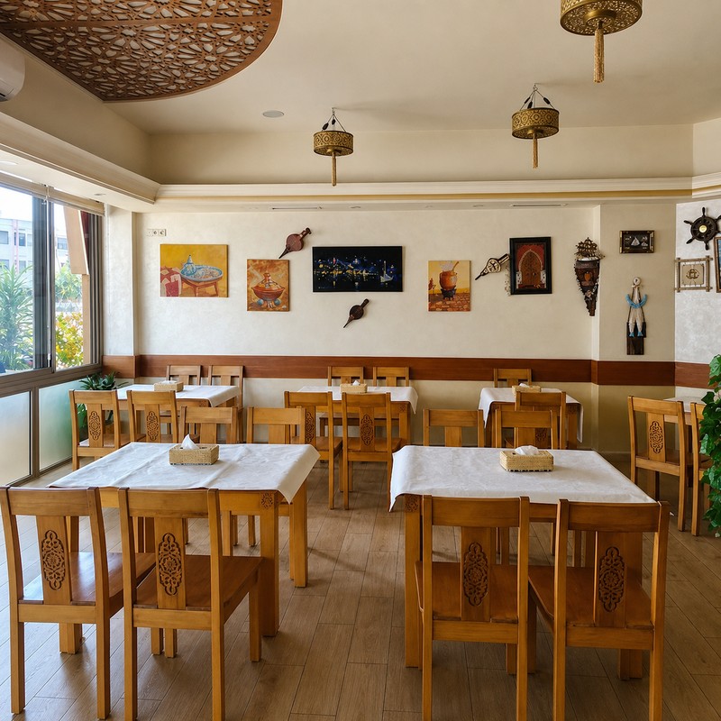 Salle de Dar Al Achab à Rabat : tables nappées de blanc, chaises en bois sculpté et plafond en moucharabieh
