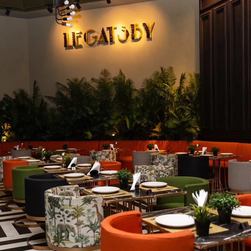 Salle du Gatsby : fauteuils orange, mur végétal et enseigne lumineuse