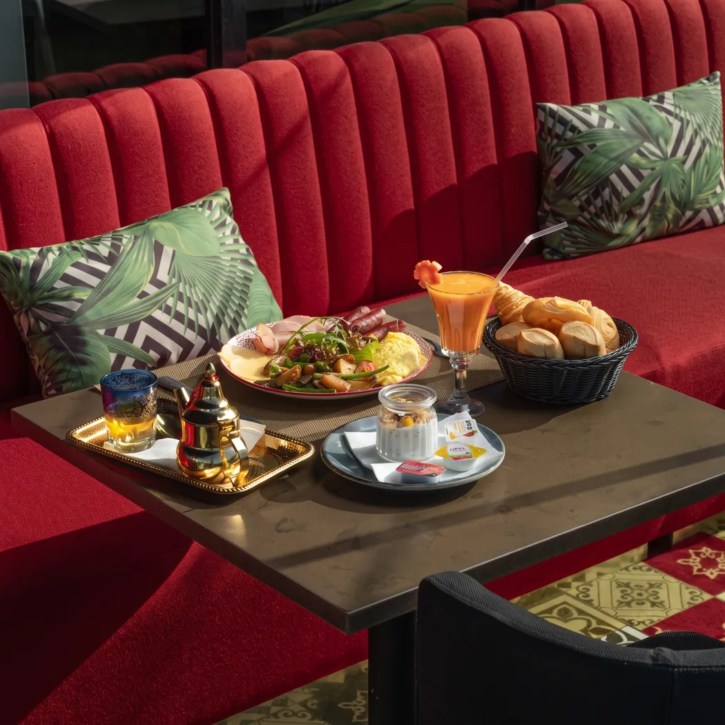 Plateau de petit-déjeuner avec thé à la menthe, jus et viennoiseries sur banquette rouge du Gatsby