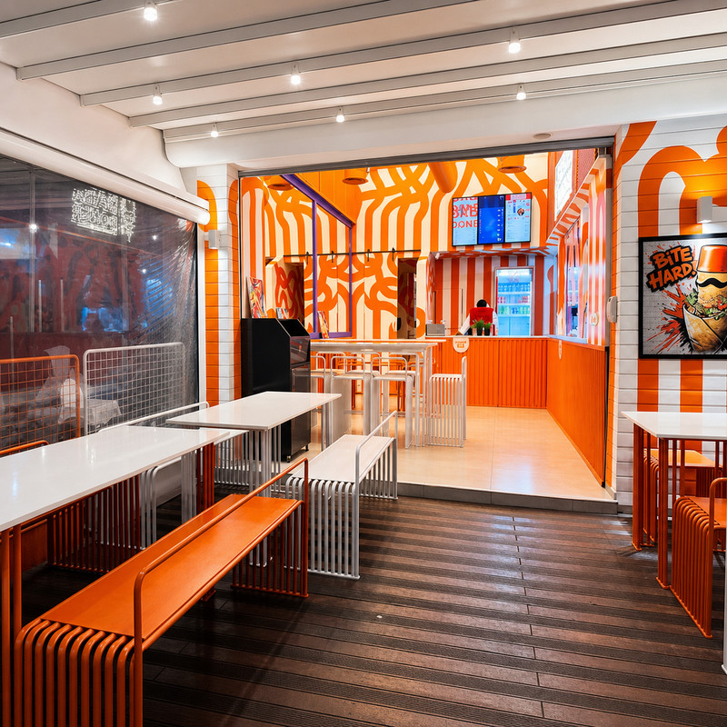 Salle de Baba Doner aux murs orange et blanc, bancs et comptoir au fond