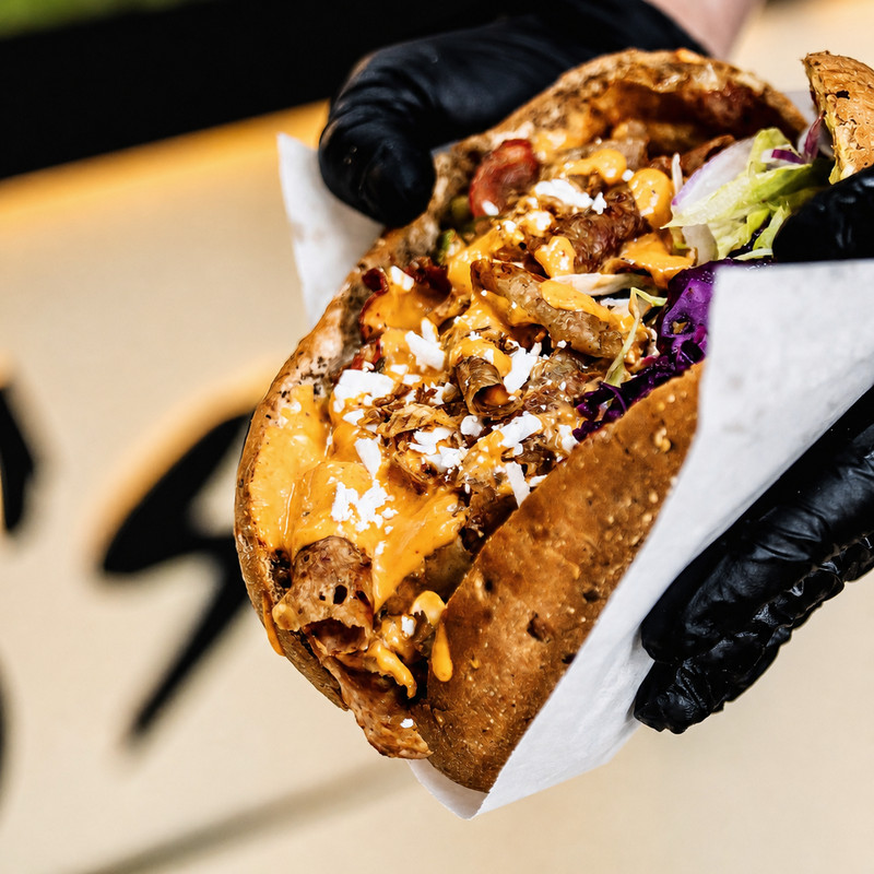 Döner de Bomo's Kebab tenu à la main, viande, chou rouge et sauce orangée