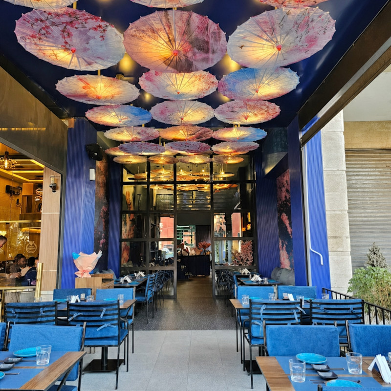 Salle de HySushi Izdihar à Marrakech : plafond d'ombrelles fleuries, murs bleus et chaises bleues