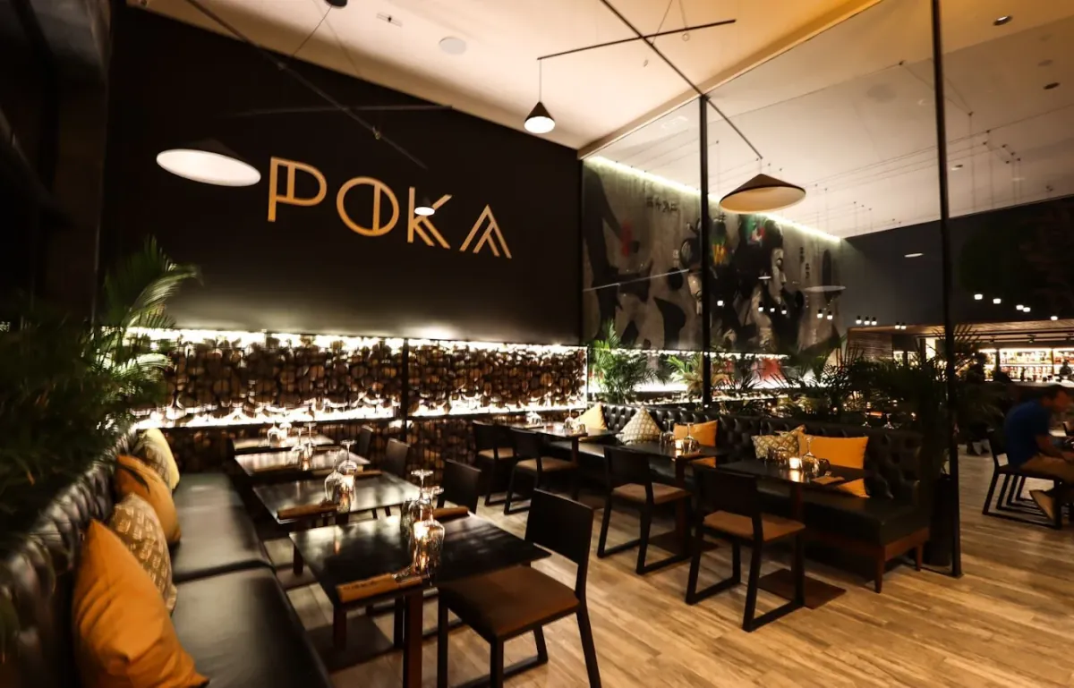 Salle en longueur de Poka by Katsura, Marrakech : banquette à coussins orange, bar éclairé et plantes
