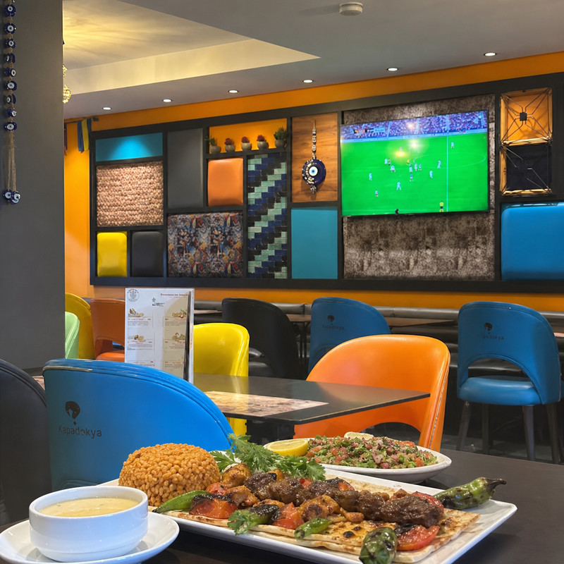 Mur décoré de carreaux colorés et écran chez Kapadokya, assiette de grillades au premier plan