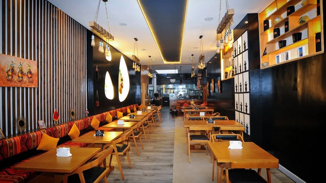 Longue salle de Dar Kasri avec banquette à coussins orange, tables en bois et mur à lattes