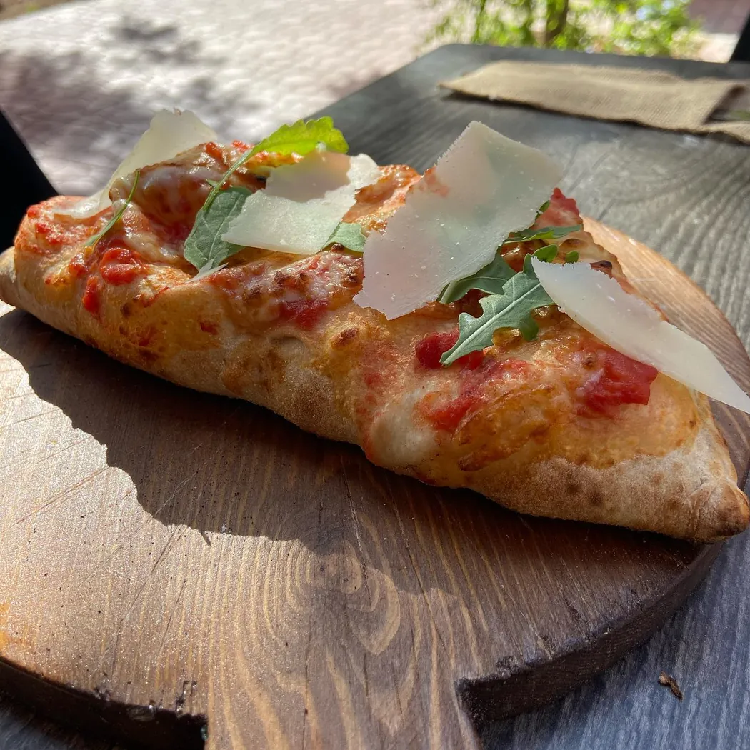 Black Pan à Marrakech : part de pizza à la roquette et copeaux de parmesan sur planche en bois
