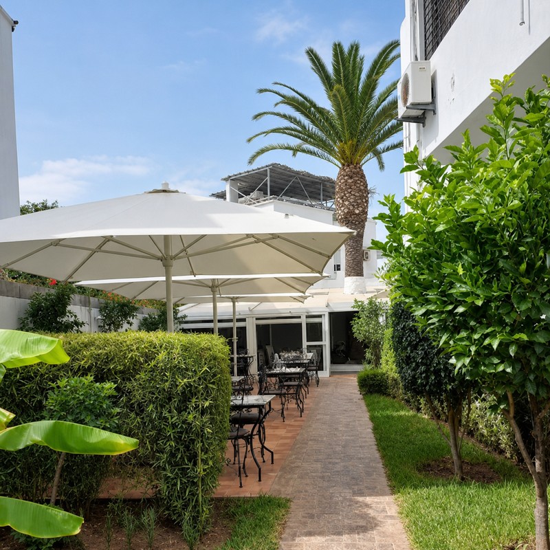 Il Giardino à Rabat : allée du jardin bordée de haies, parasols blancs et palmier