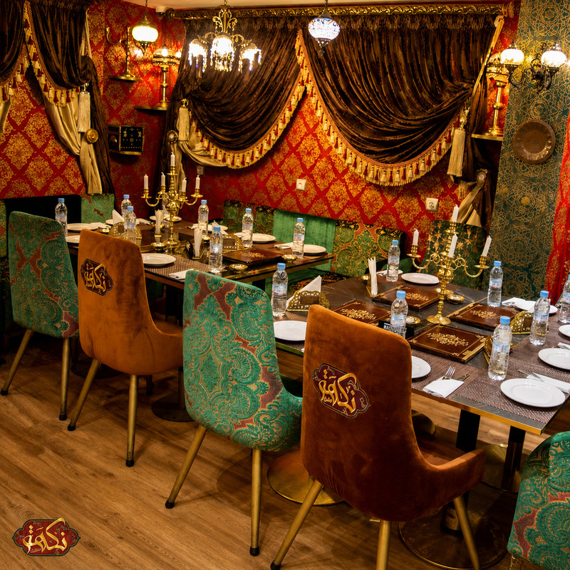 Salle de Nakhat Chef Nour : tentures rouges, lustres et fauteuils en velours vert et cuivre