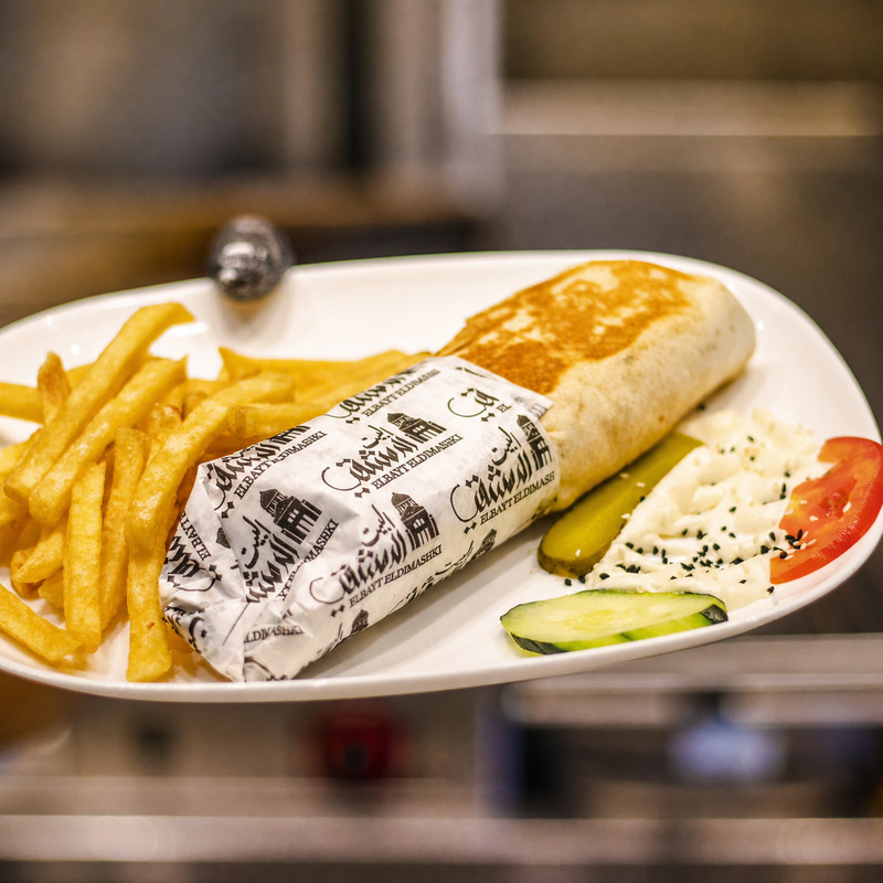 Sandwich shawarma emballé, frites, cornichons et sauce blanche servis chez El Bayt El Dimashki