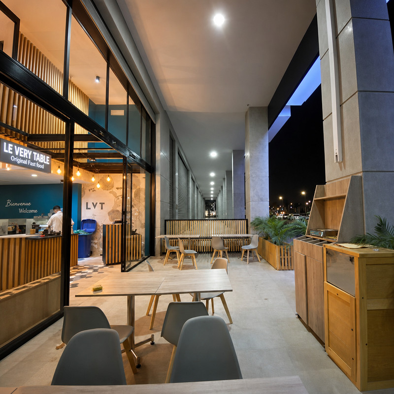 Terrasse couverte de Le Very Table à Agadir Bay, tables en bois et enseigne lumineuse le soir