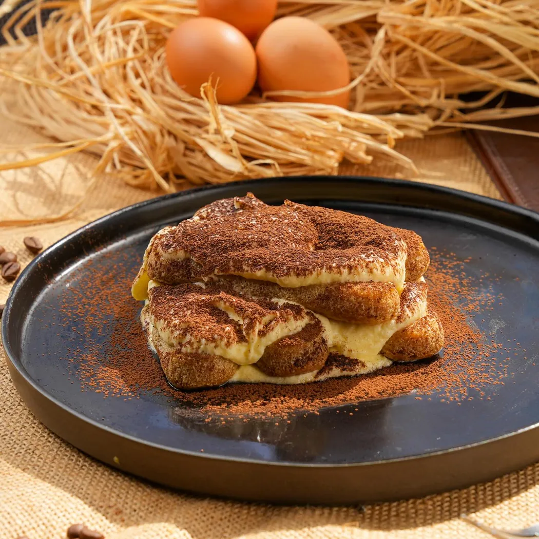 Latium à Rabat : part de tiramisu saupoudrée de cacao sur une assiette noire
