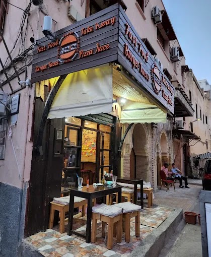 Façade de 212pizzeria dans une ruelle de la médina de Fès, avec tabourets et tables en terrasse