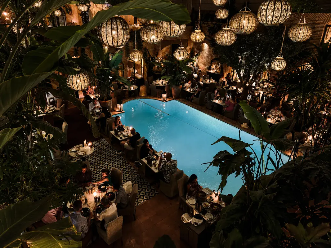 La Trattoria à Marrakech : tables dressées de nuit autour de la piscine, sous des lanternes et des palmiers