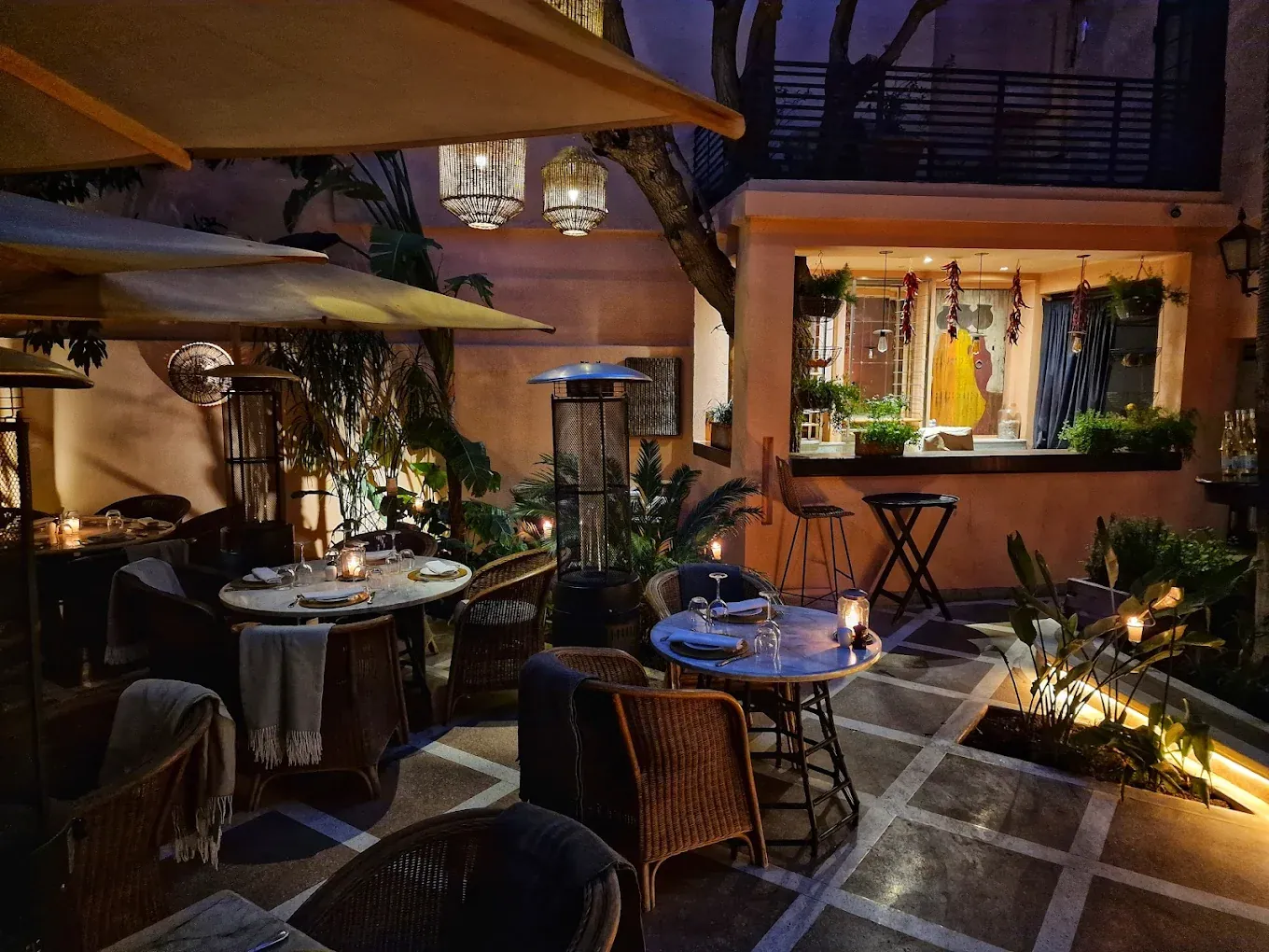 La Trattoria à Marrakech : terrasse éclairée le soir, tables rondes et fauteuils en rotin