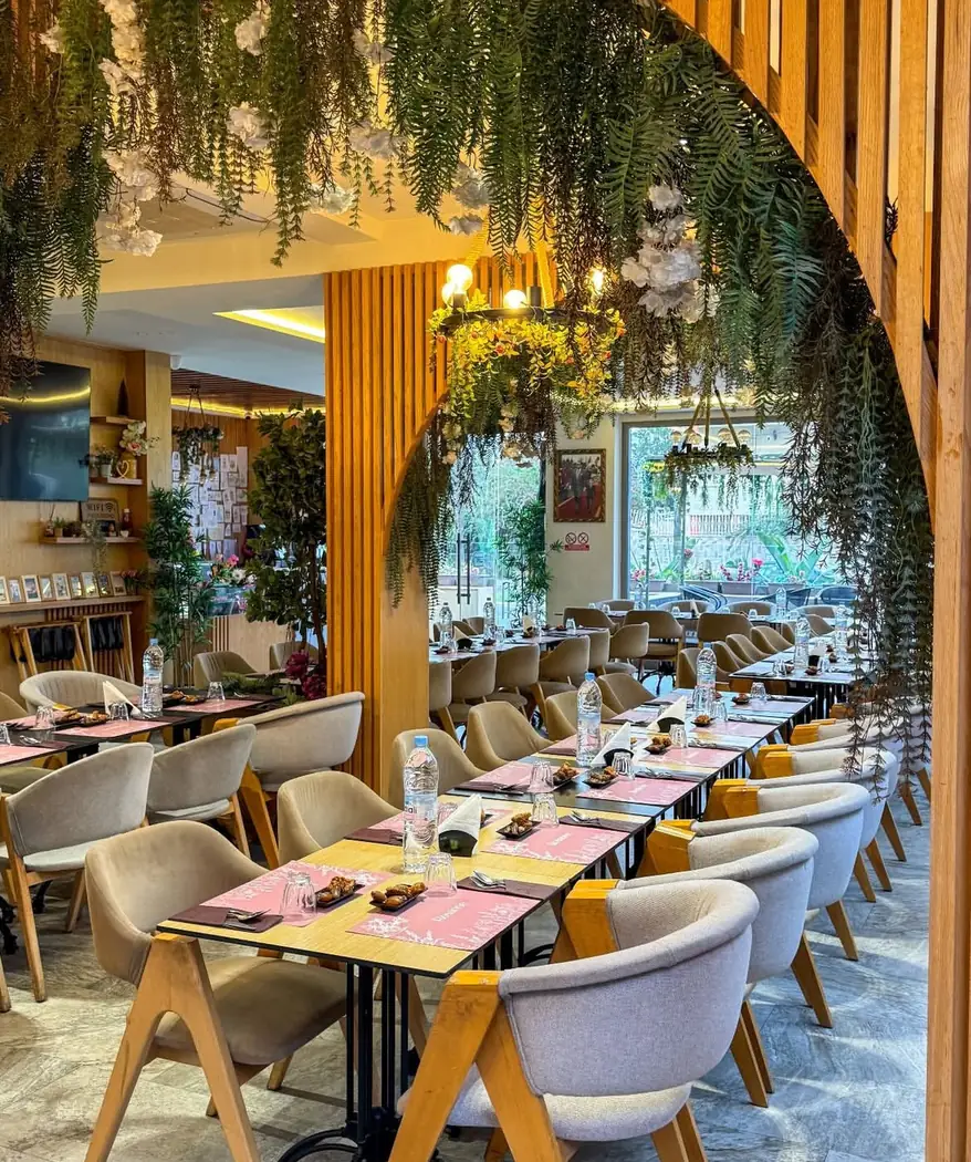 Salle de Rosanne sous une arche fleurie, tables en bois et fauteuils beiges
