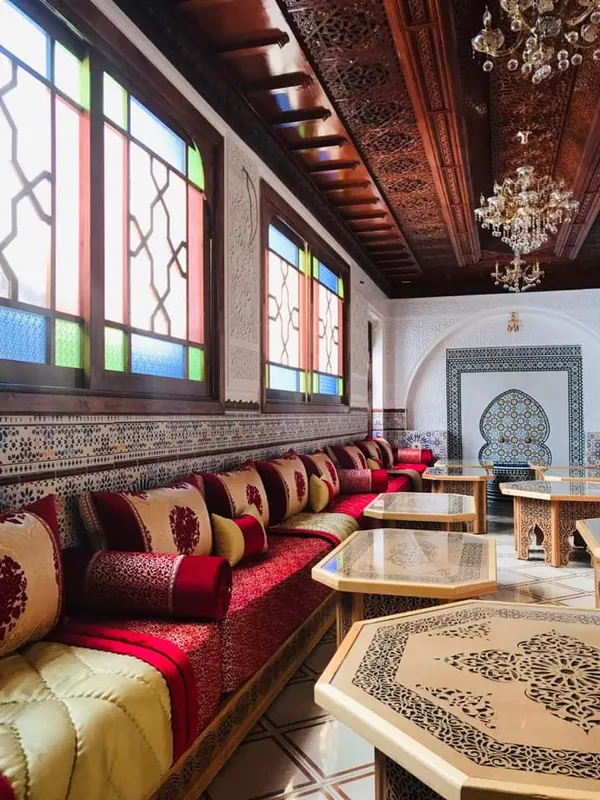Salon de Riad Al Andalous à Tanger : banquettes rouges et dorées, vitraux et plafond en bois sculpté