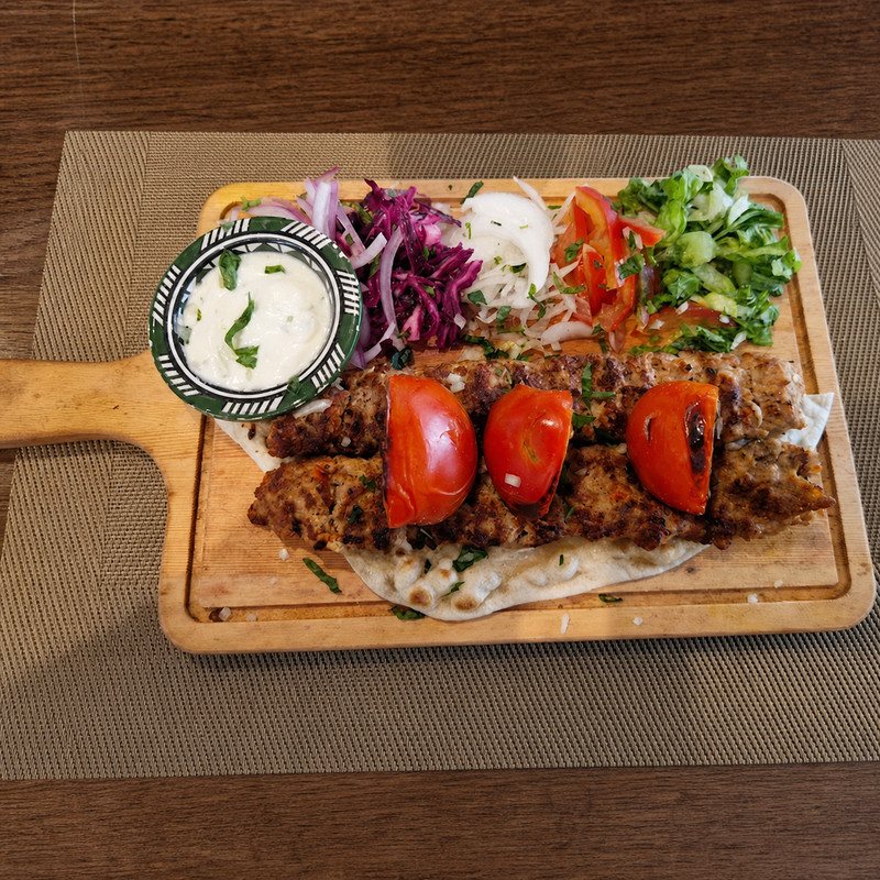 Brochettes de kebab grillées, tomates, oignons et sauce blanche sur planche en bois chez Kabab Erbil