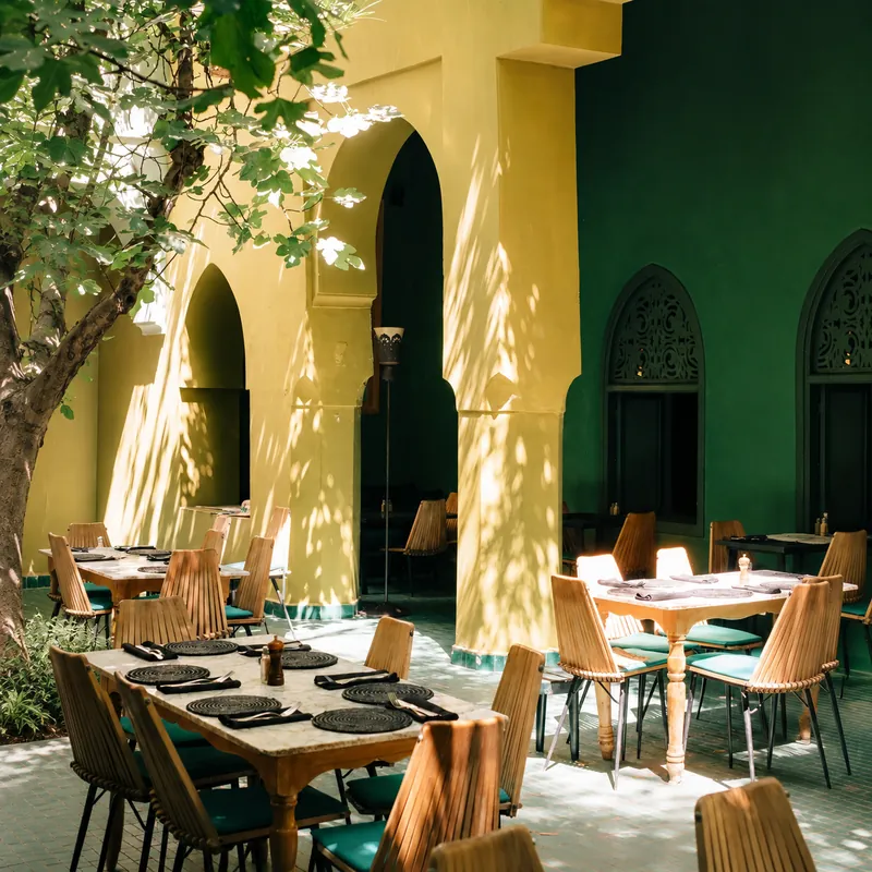 Tables en bois sous les arcades jaunes et vertes du Jardin