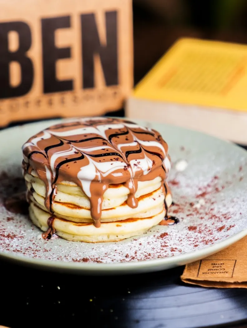 Pile de pancakes nappés de chocolat au lait et blanc, devant un sachet de café O'Ben