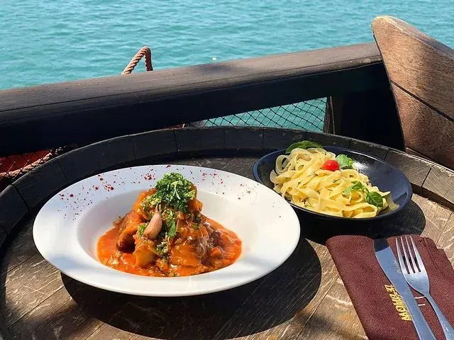 Plat en sauce et tagliatelles servis au bord du pont du Dhow, face à l'eau