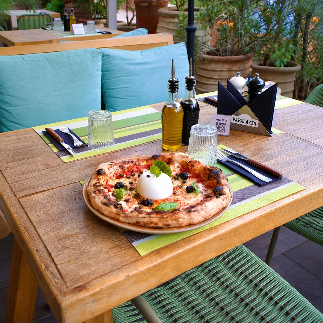 Papàlazzo à Marrakech : pizza à la burrata sur une table en bois en terrasse, coussins bleus