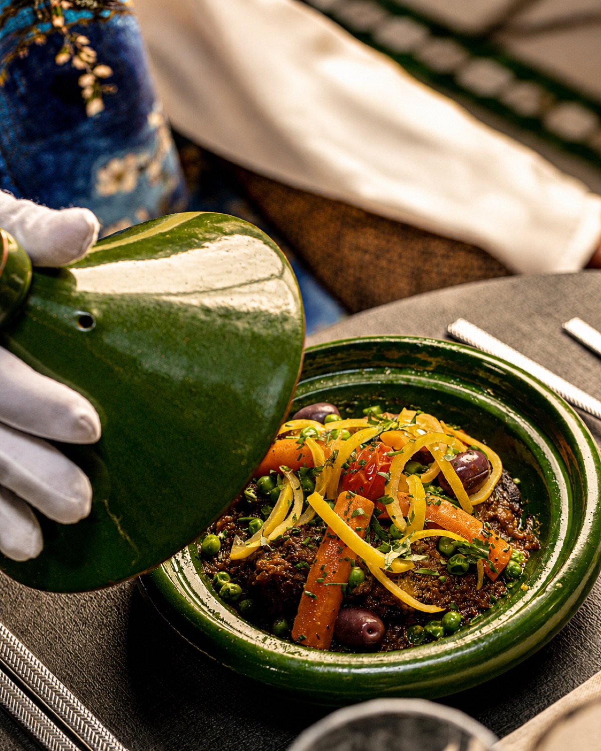 Serveur ganté soulevant le couvercle d'un tajine aux légumes chez Dar Dada