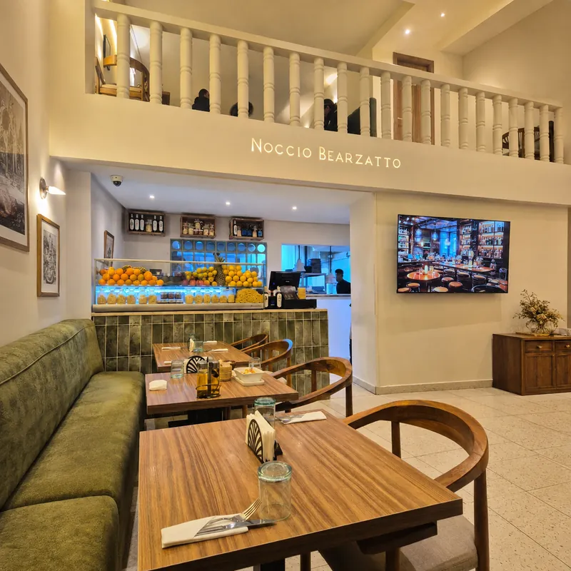Noccio Bearzatto à Marrakech : salle claire avec mezzanine, banquette verte et tables en bois