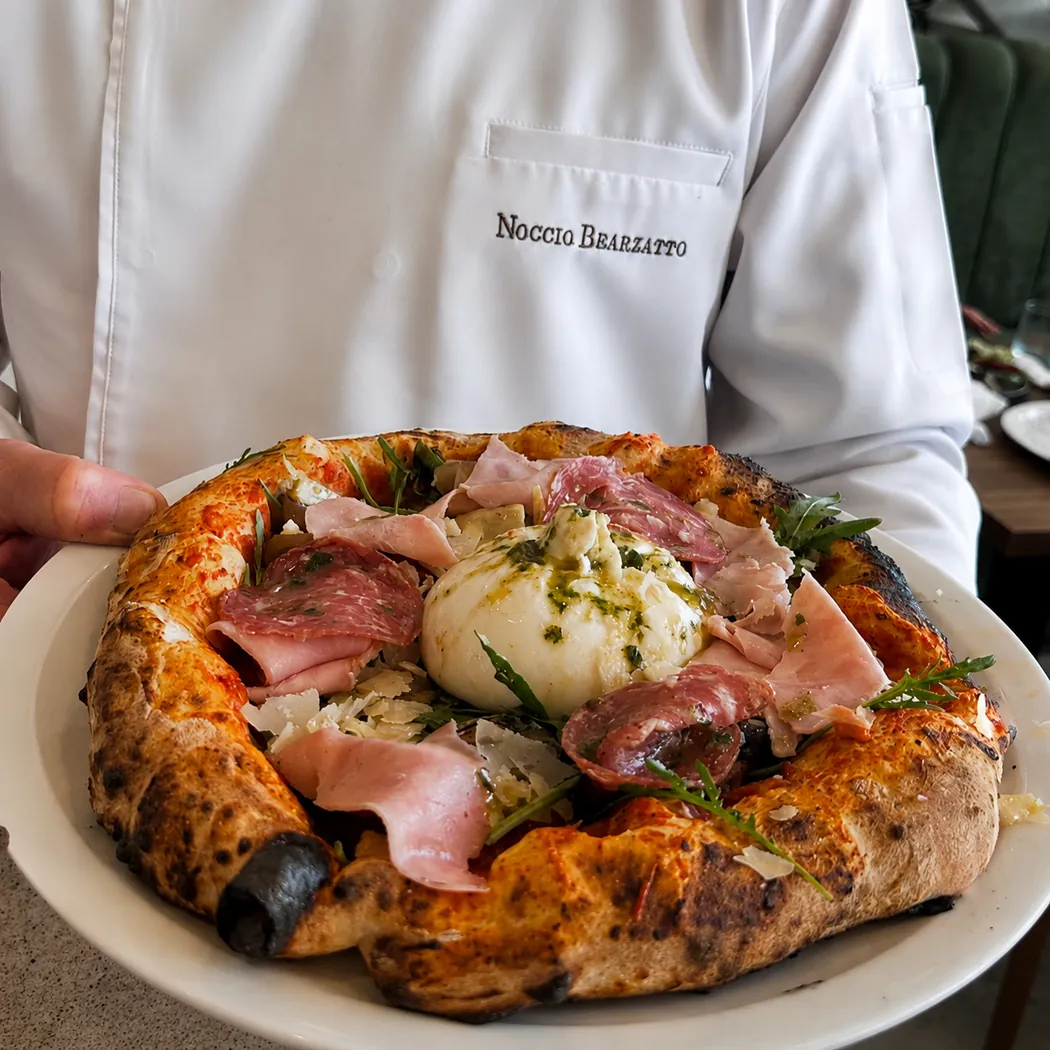 Noccio Bearzatto à Marrakech : pizza à bord gonflé garnie de burrata et de charcuterie, tenue par un serveur