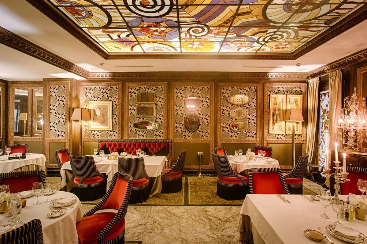 Salle du Jasmine à Casablanca sous une verrière colorée Art déco, fauteuils rouges et tables nappées