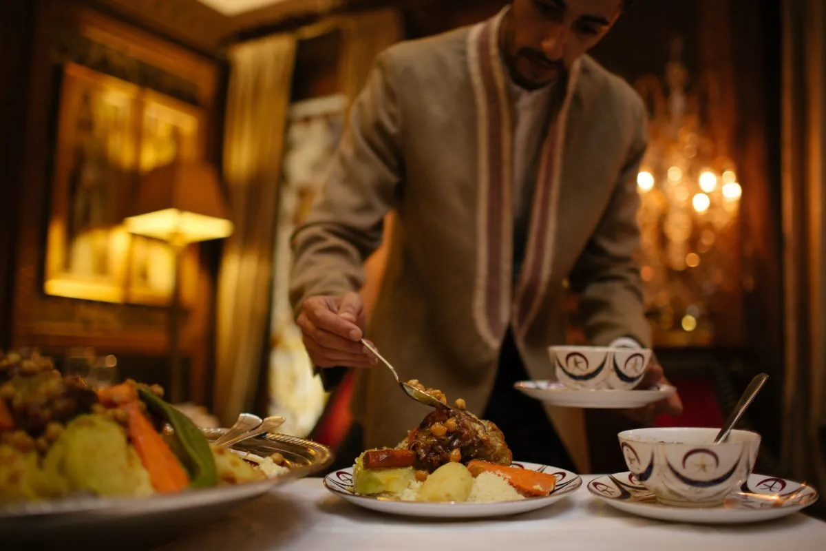 Serveur en tenue traditionnelle servant un couscous aux légumes au Jasmine