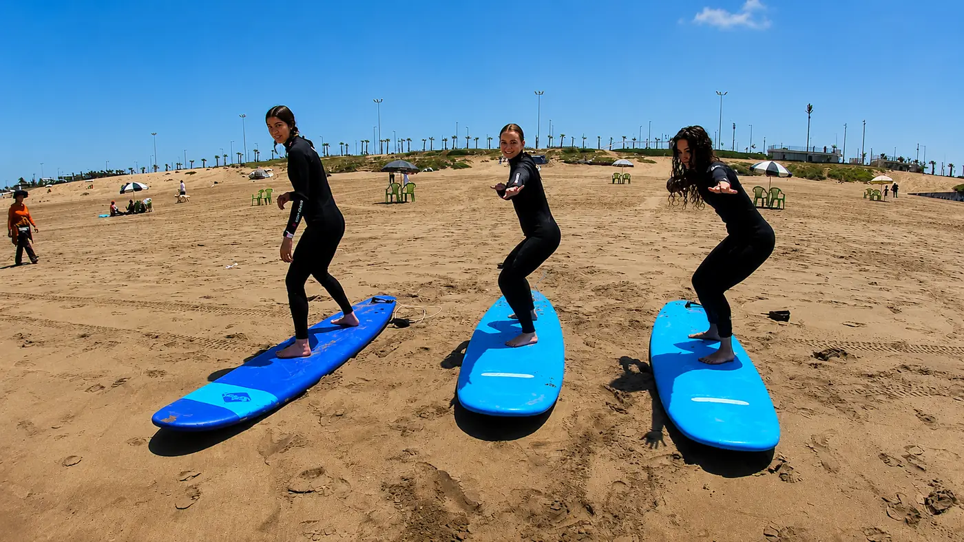 Trois élèves de Casablanca Surf Coaching s'entraînent au take-off sur le sable d'Aïn Diab