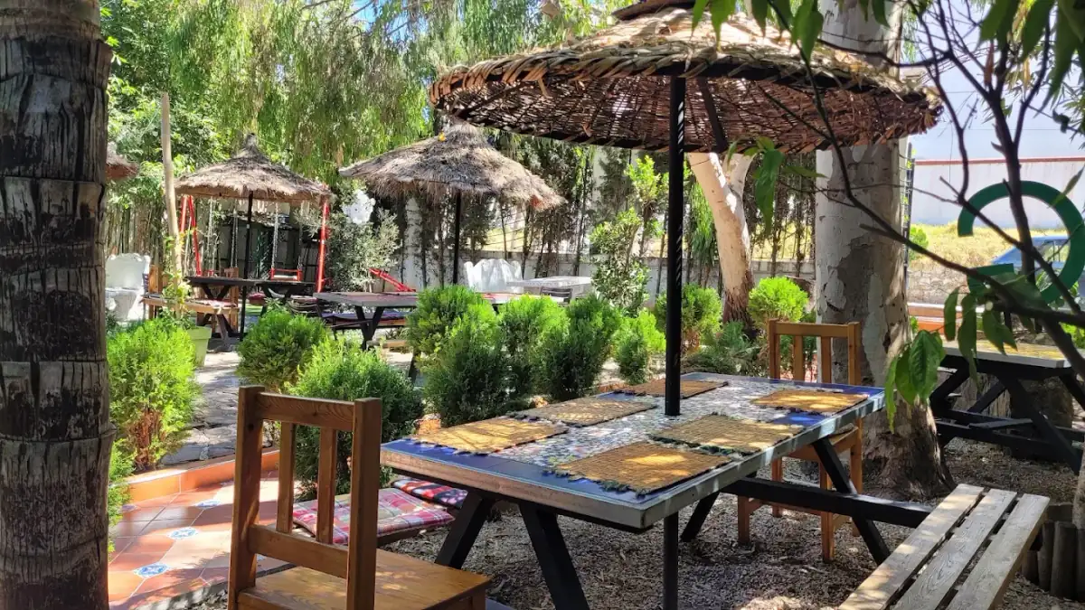 Jardin de Villa Al Achab à Tanger : tables en bois, parasols de paille et verdure