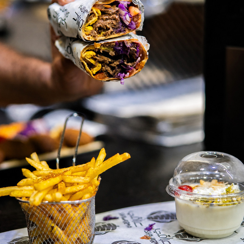 Deux wraps shawarma garnis de chou rouge tenus au-dessus d'un panier de frites chez Iraki Shawarma