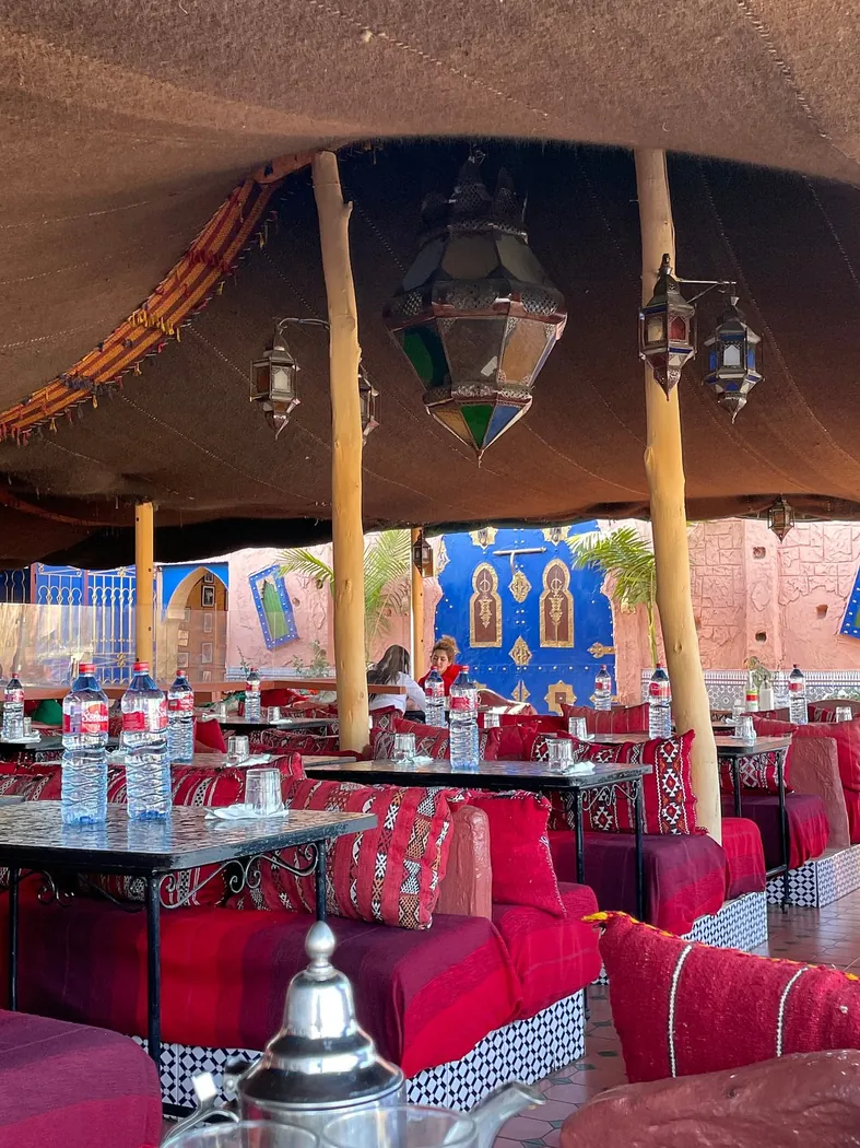 Terrasse couverte de Dar Naji avec banquettes rouges, lanternes en cuivre et tables en zellige
