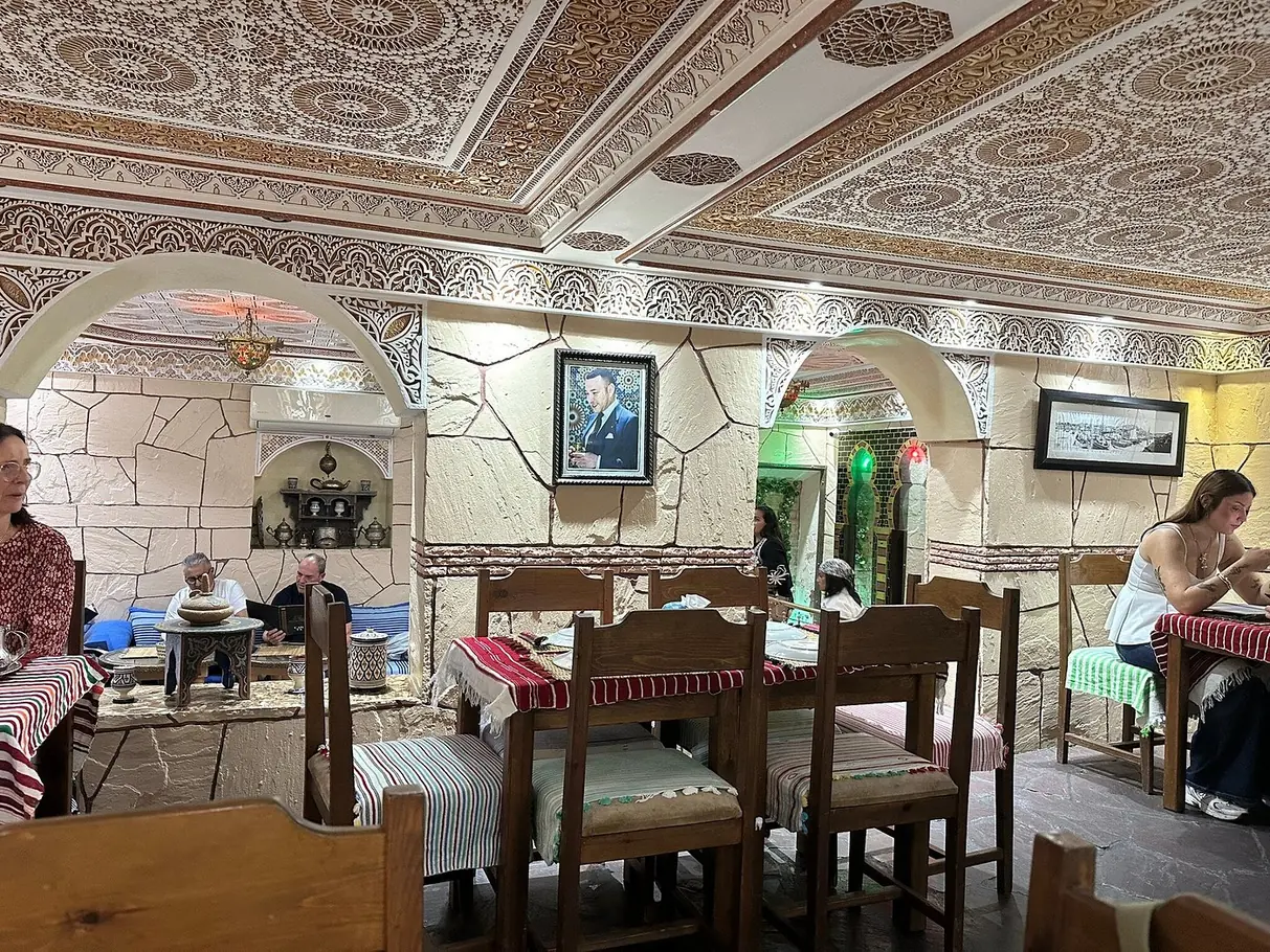 Salle de Maison Grill Kasbah à Tanger sous un plafond en plâtre sculpté, tables nappées de rouge