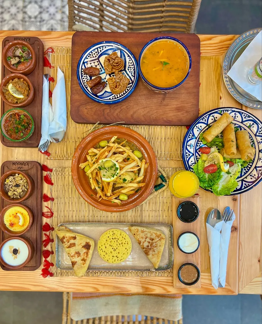 Vue du dessus d'une table de Kamoun : tajine, salades, briouates et jus d'orange