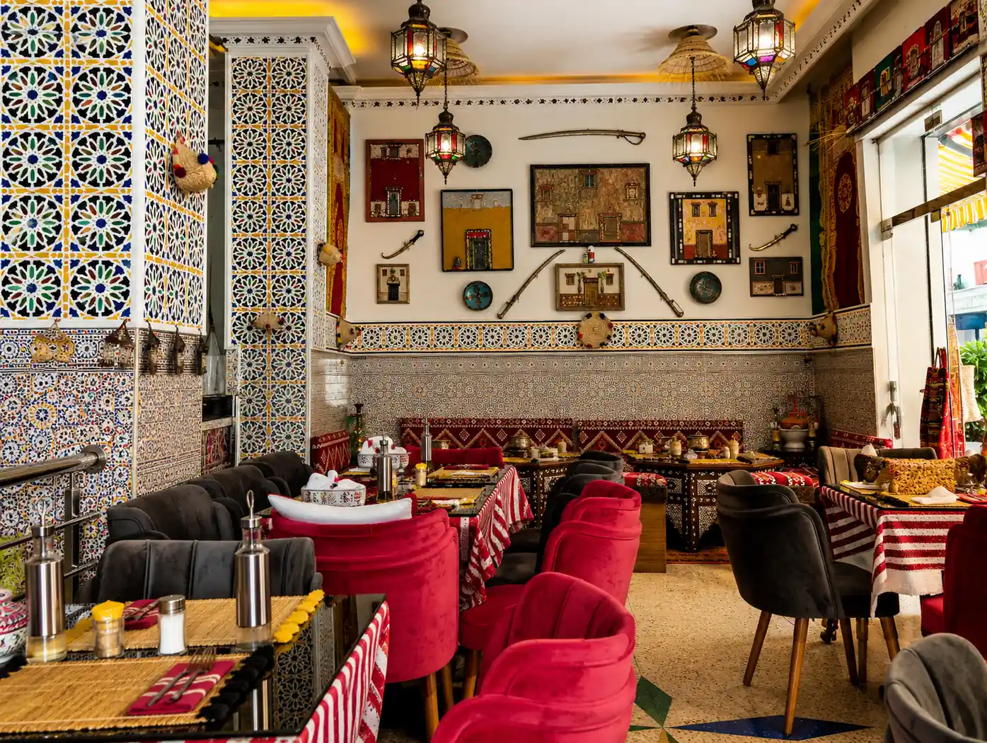Tables du restaurant Cheikh Ibrahim sous des lanternes en cuivre, murs décorés de tableaux