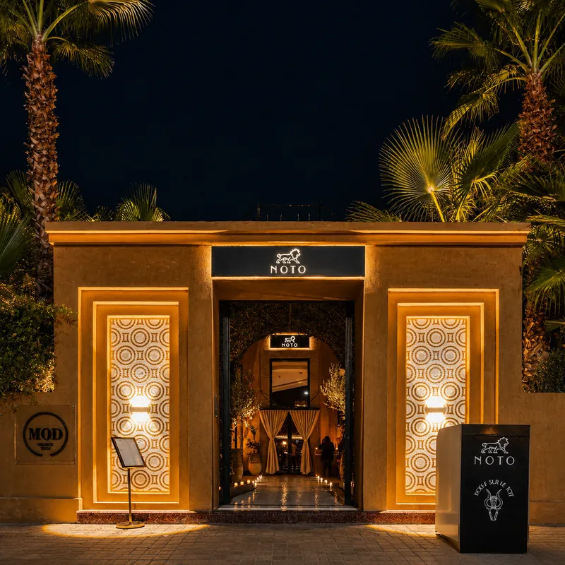 Noto à Marrakech : façade éclairée de nuit, entrée encadrée de palmiers