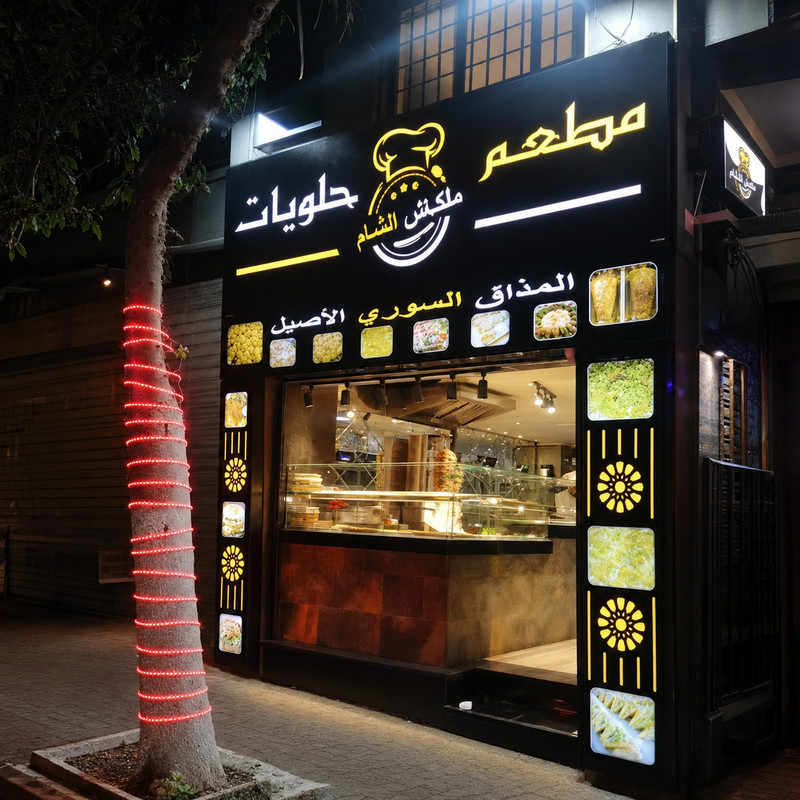 Façade de Melkash alsham rue de Fès, enseigne en arabe et vitrine éclairée le soir